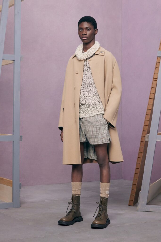 An oversized beige coat paired with fitted plaid shorts, creating a stylish layered look.