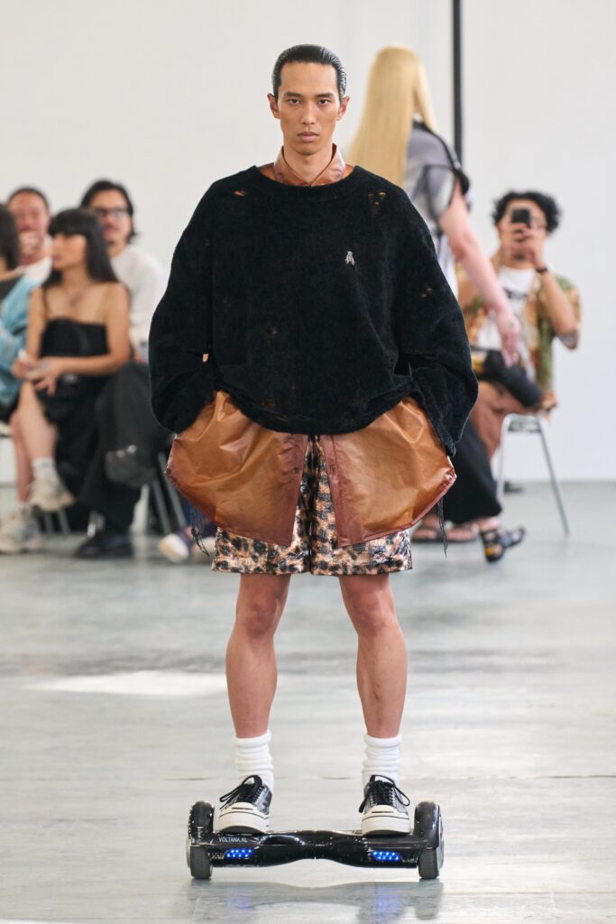 A relaxed black long-sleeve top paired with layered brown shorts featuring an asymmetric design.