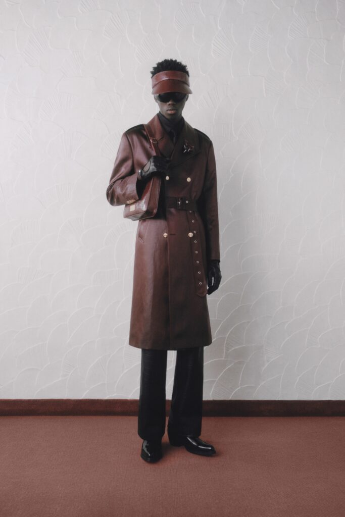 A fitted brown leather coat with a collared neckline and buttoned detail paired with fitted pants.