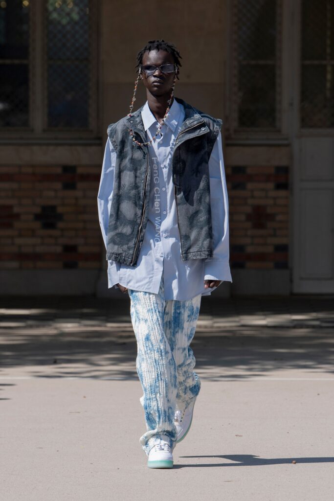 A relaxed fit blue denim vest layered over a collared long-sleeve shirt.