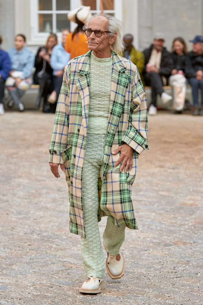 A relaxed beige checked coat layered over a green jumpsuit with long sleeves.