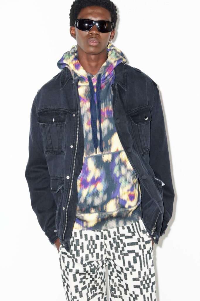 A relaxed black denim jacket layered over a multicolor printed hoodie.