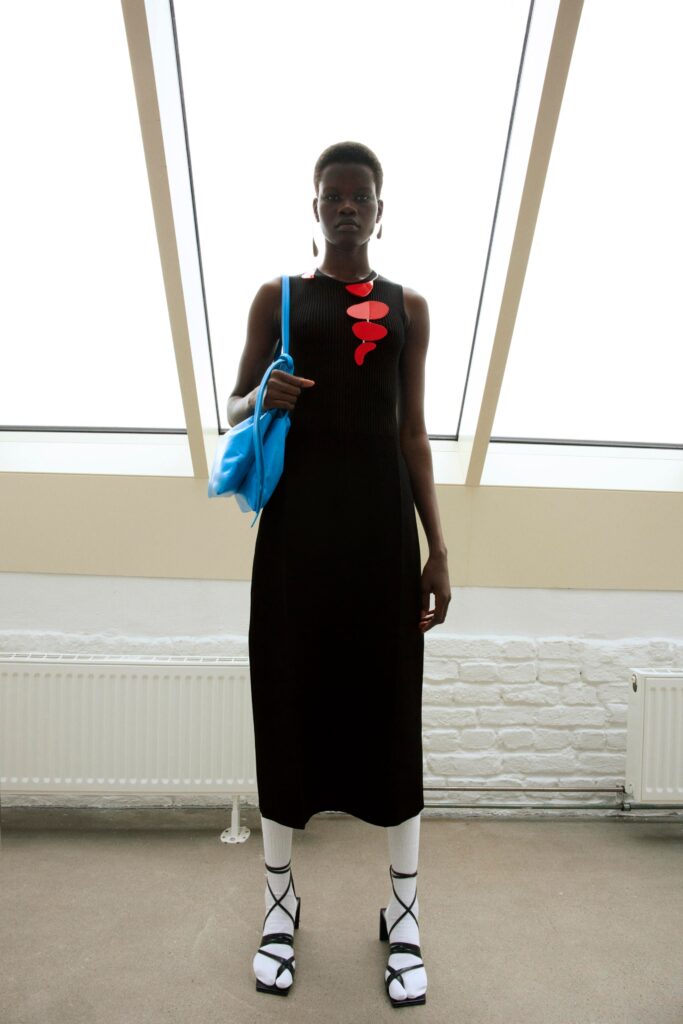 A fitted black cotton sleeveless dress with a high neckline and straight-leg silhouette.