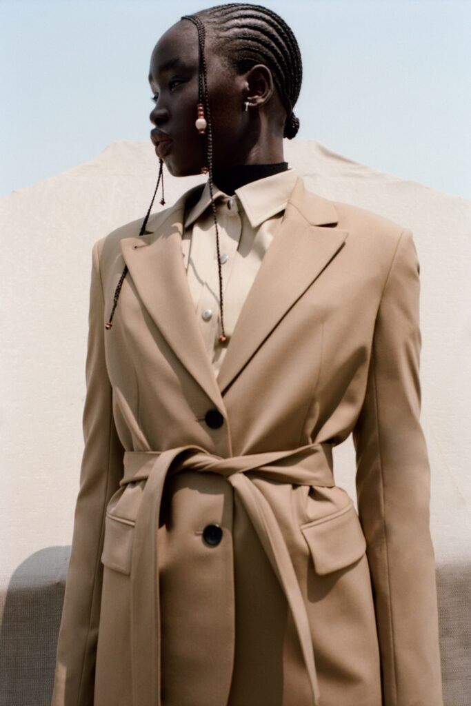 A tailored beige blazer with a collared shirt, featuring a belted design detail.