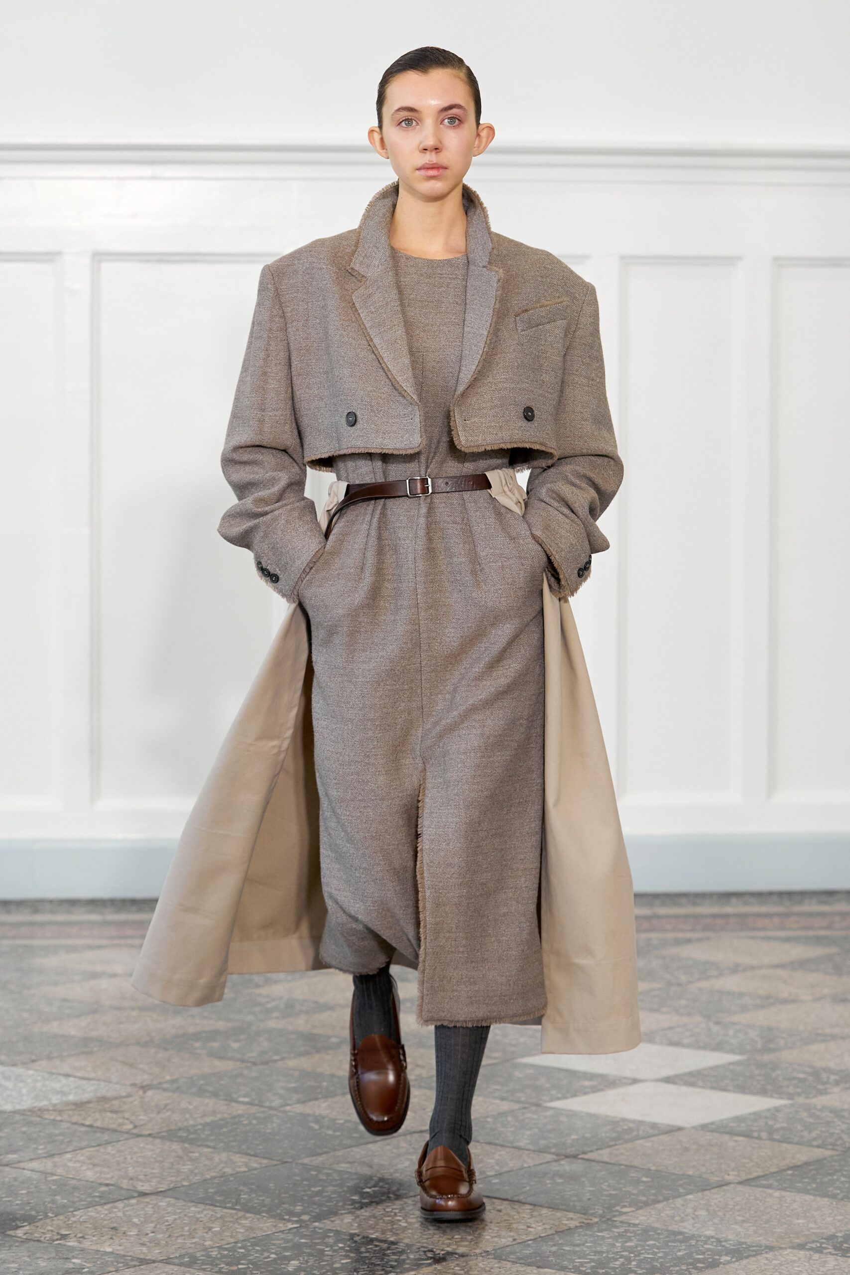 A fitted brown wool coat dress with long sleeves and a belted waist, featuring an asymmetric design.