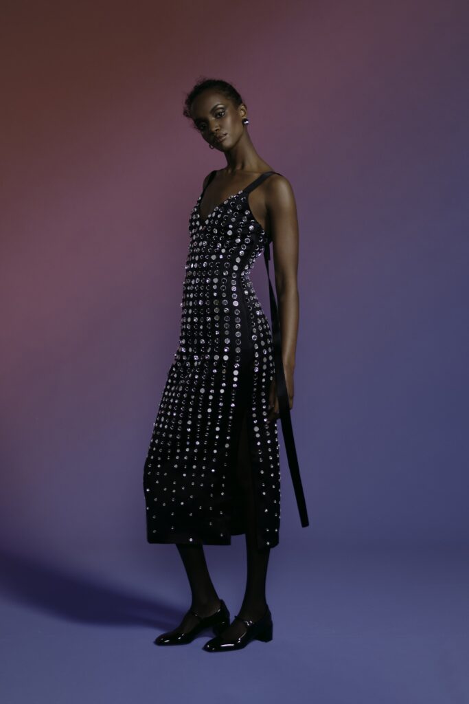 A fitted black sleeveless dress with a V-neckline and sequined detail featuring a slit.