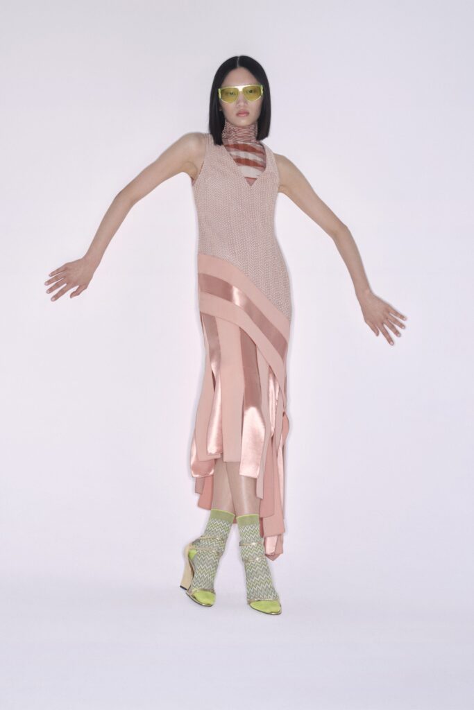A fitted pink silk sleeveless dress with a V-neckline and asymmetric design.