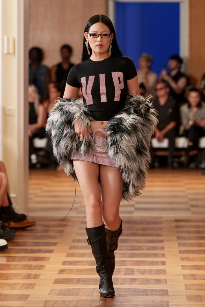 A black cropped sleeveless top paired with a pink mini skirt and a faux-fur coat.