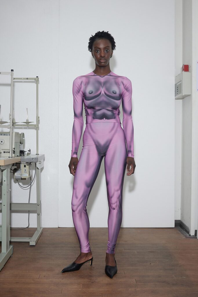 A fitted pink cotton catsuit with long sleeves and a high neck, featuring a unique printed design.