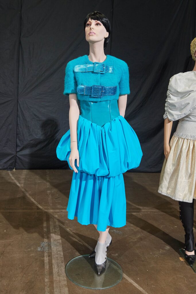 A fitted blue sleeveless dress with a high neckline and pleated design.