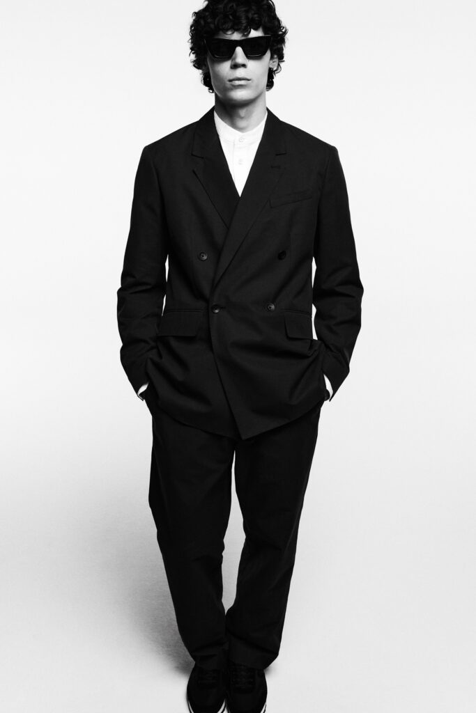 A tailored black suit with long sleeves and a collared shirt underneath.