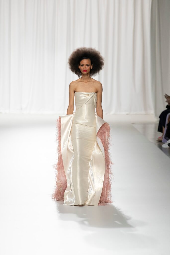 A fitted cream silk strapless gown with draped details and pink accents.