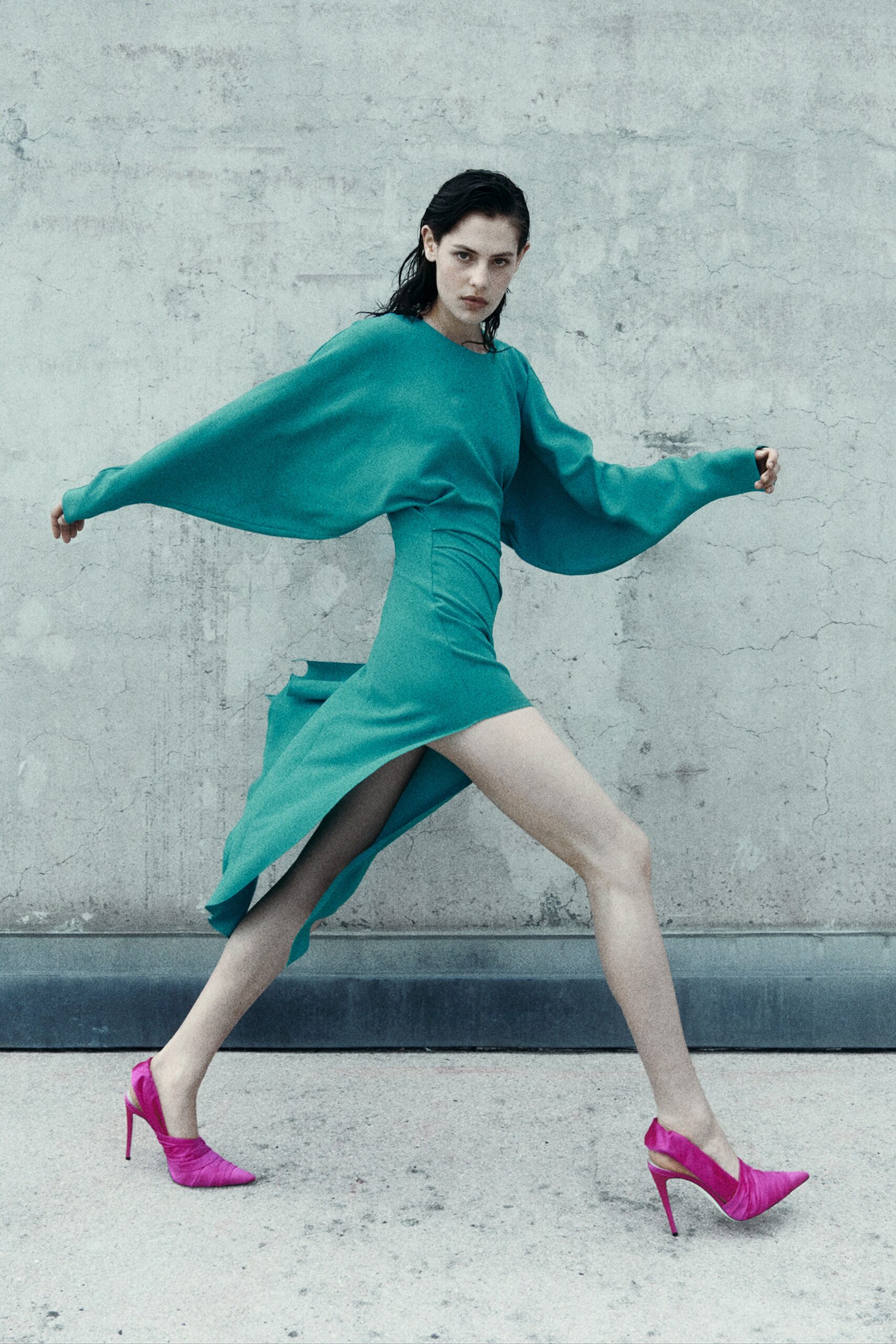 A fitted blue silk dress with long sleeves, high neckline, and an asymmetric slit detail.