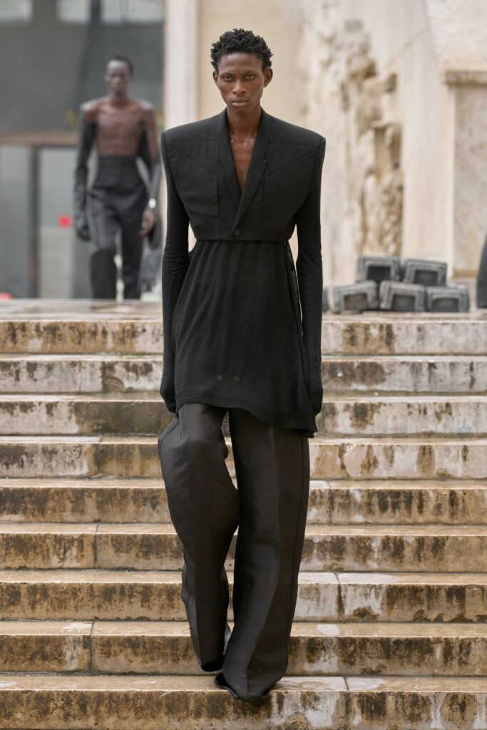 A fitted black dress with long sleeves and a collared neckline, paired with wide-leg pants.