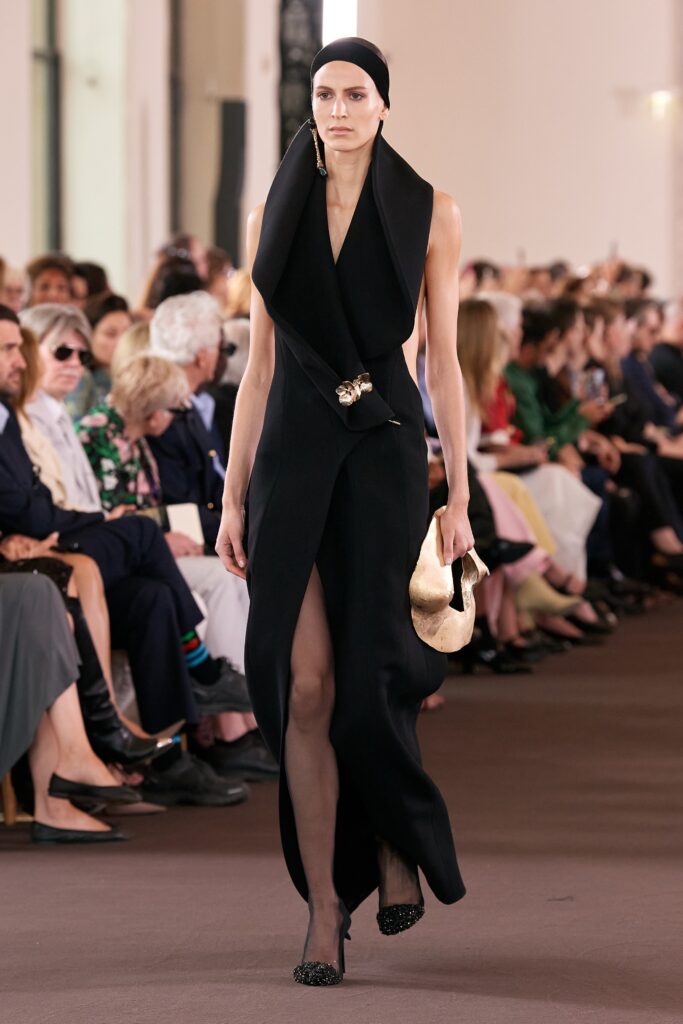 A fitted black silk sleeveless dress with a V-neckline and asymmetric slit detail.