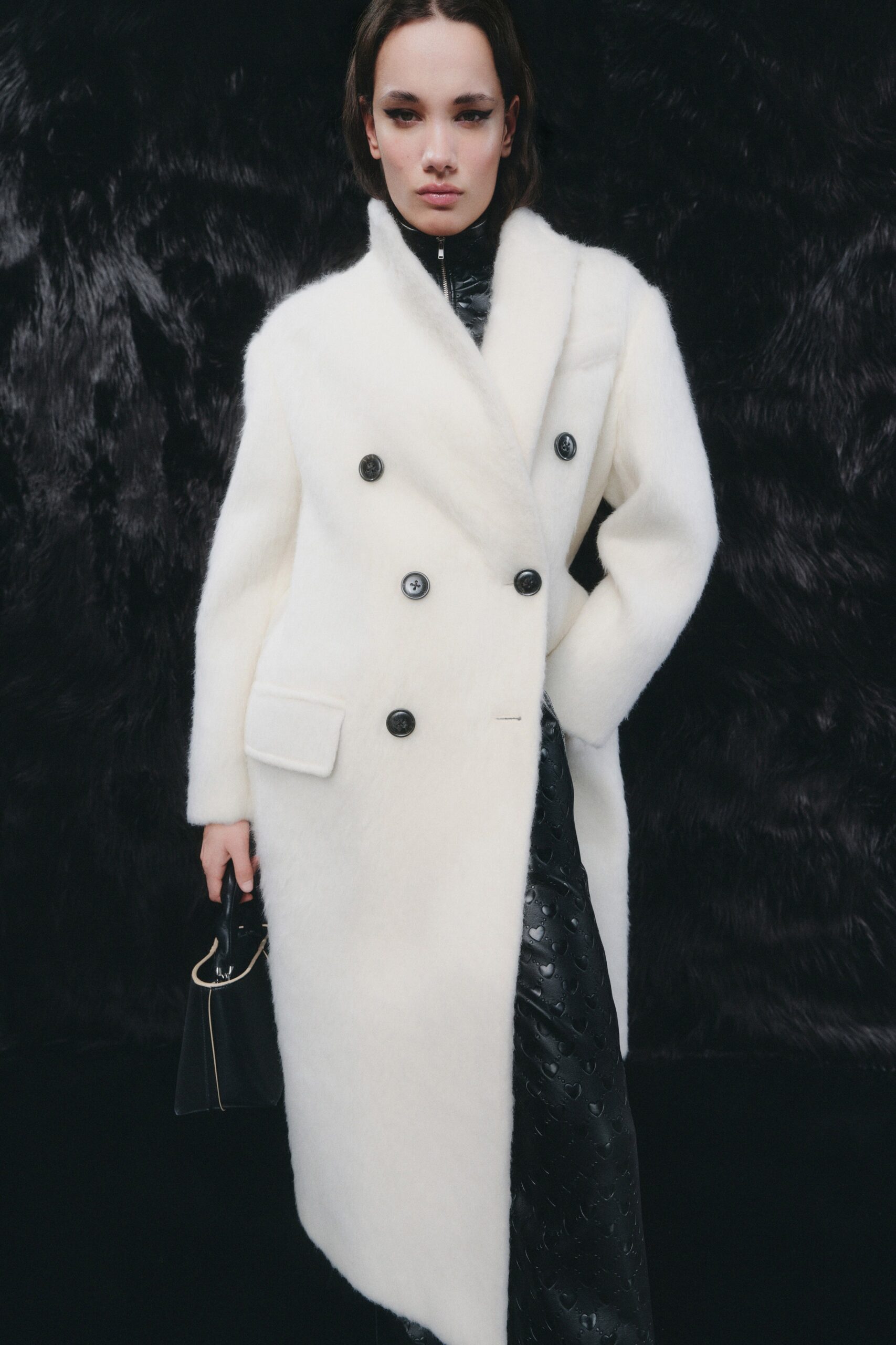 A fitted white wool coat layered over a black leather dress with a double-breasted design.