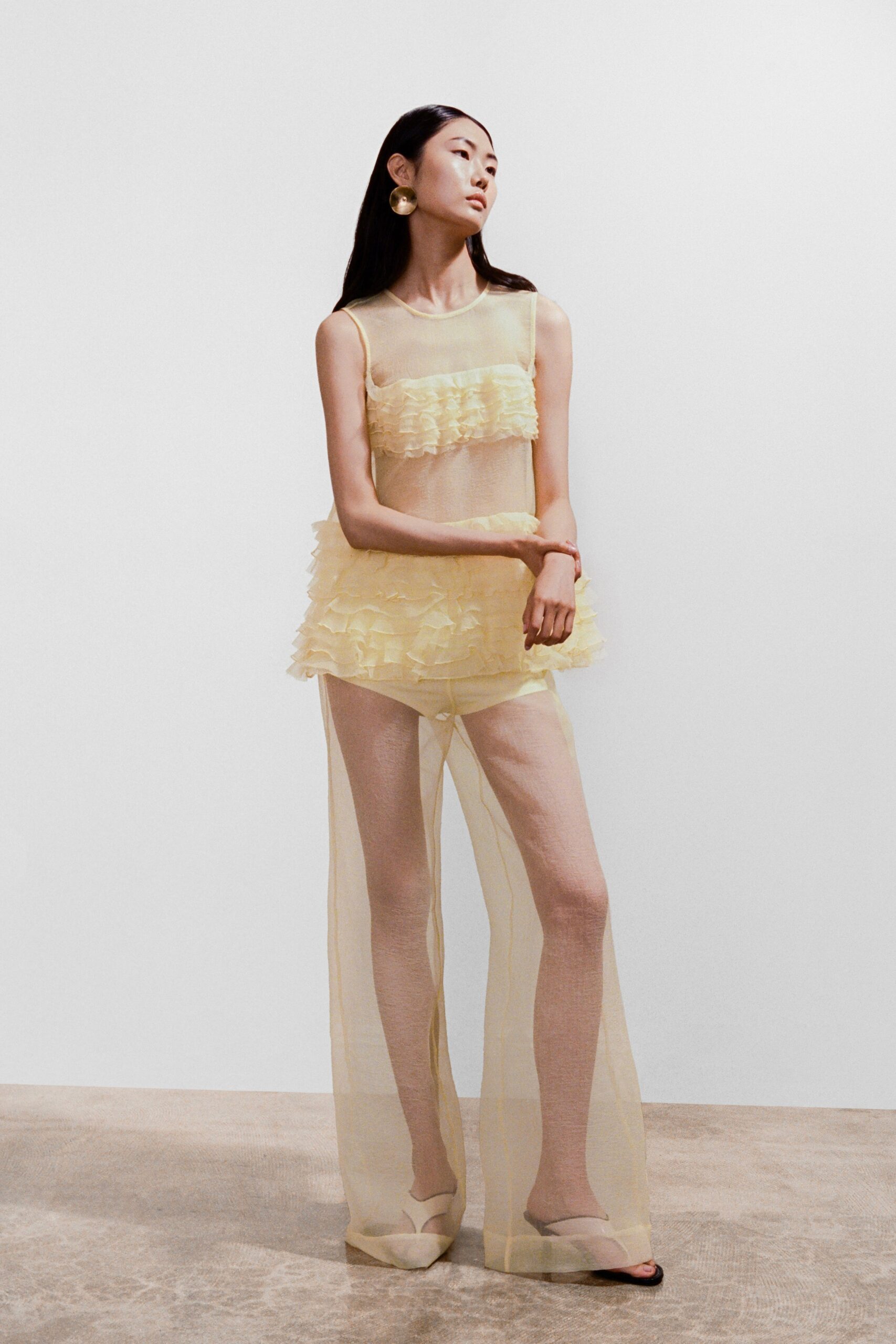 A relaxed yellow sheer sleeveless top with ruffles paired with wide-leg sheer pants.