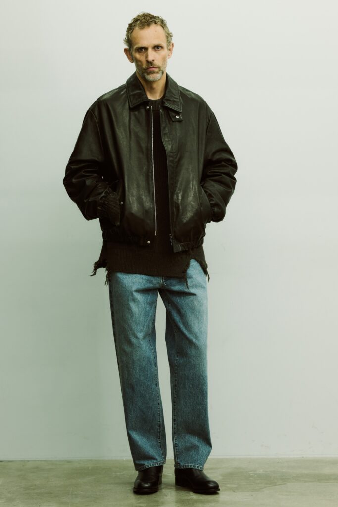 An oversized black leather jacket paired with straight-leg blue denim pants.