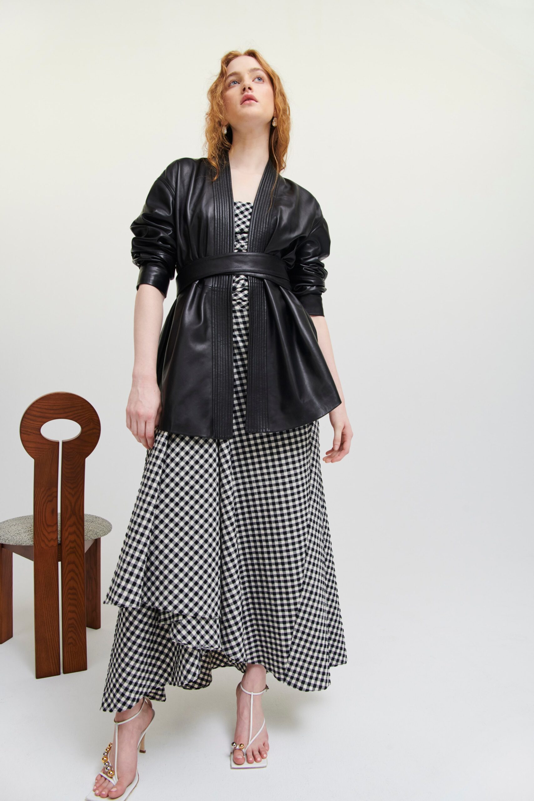 This striking ensemble features a fitted black leather jacket layered over a flowing checkered dress. The asymmetric hemline of the dress adds dynamic movement, while the v-neckline of both pieces creates a cohesive silhouette that draws the eye.