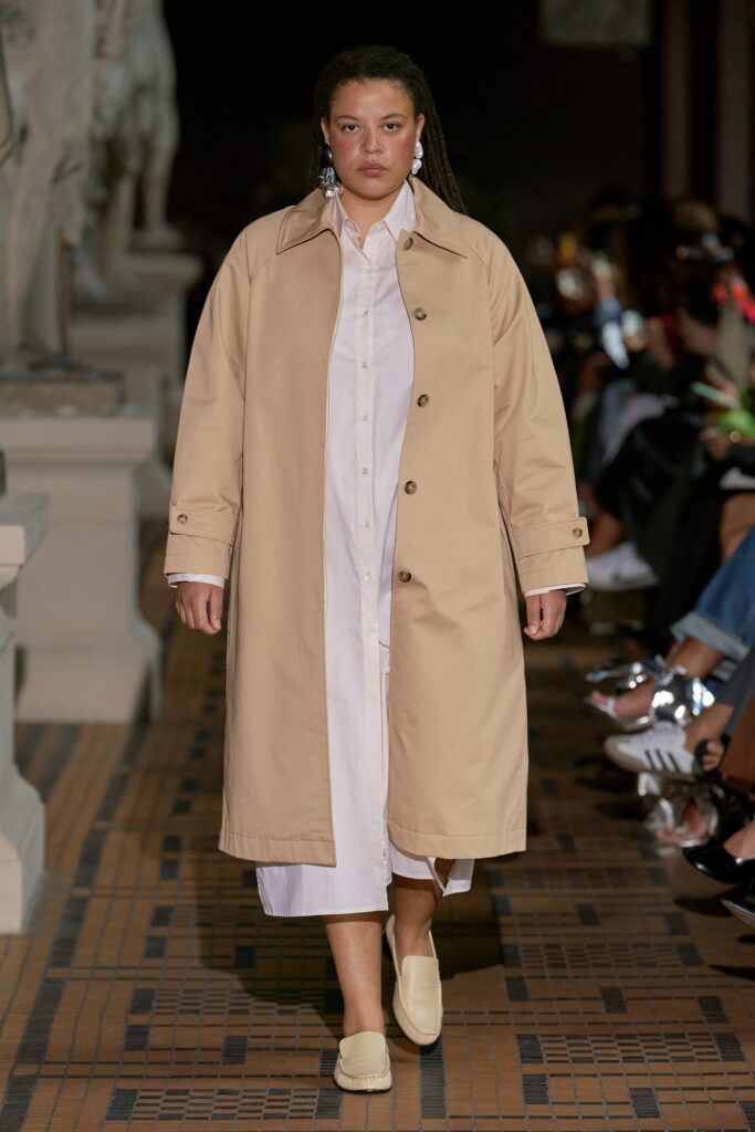 A relaxed beige coat layered over a white collared dress with buttoned details.