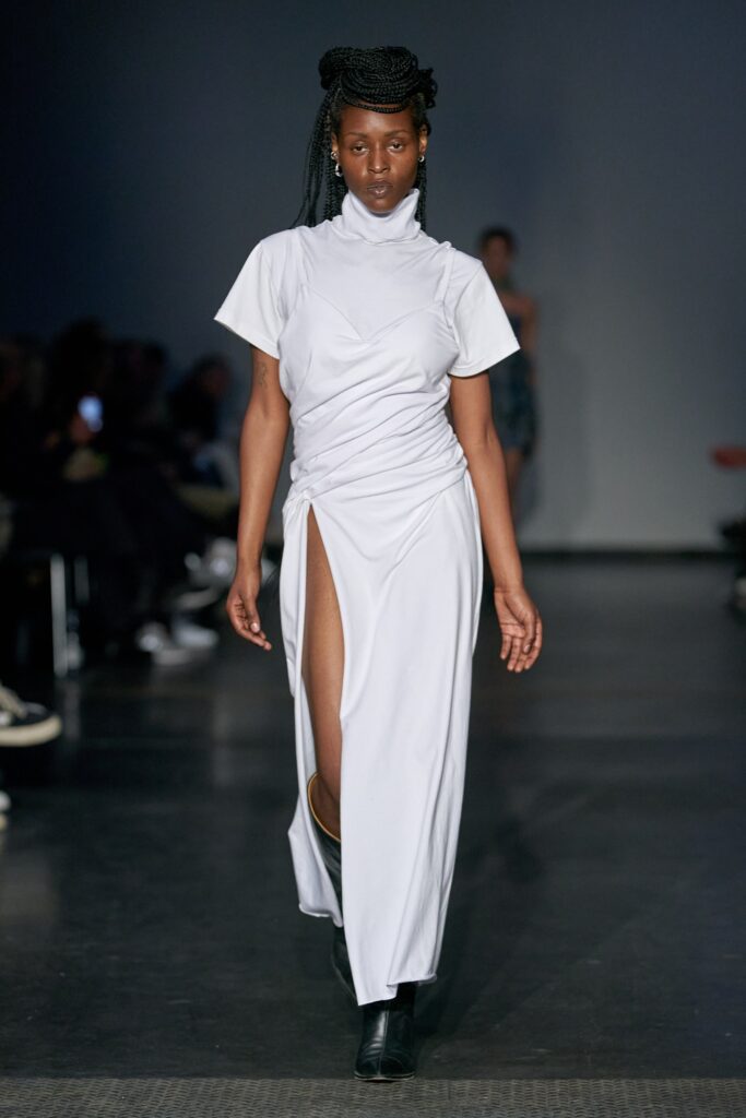A fitted white dress with short sleeves, high neckline, and an asymmetric slit detail.