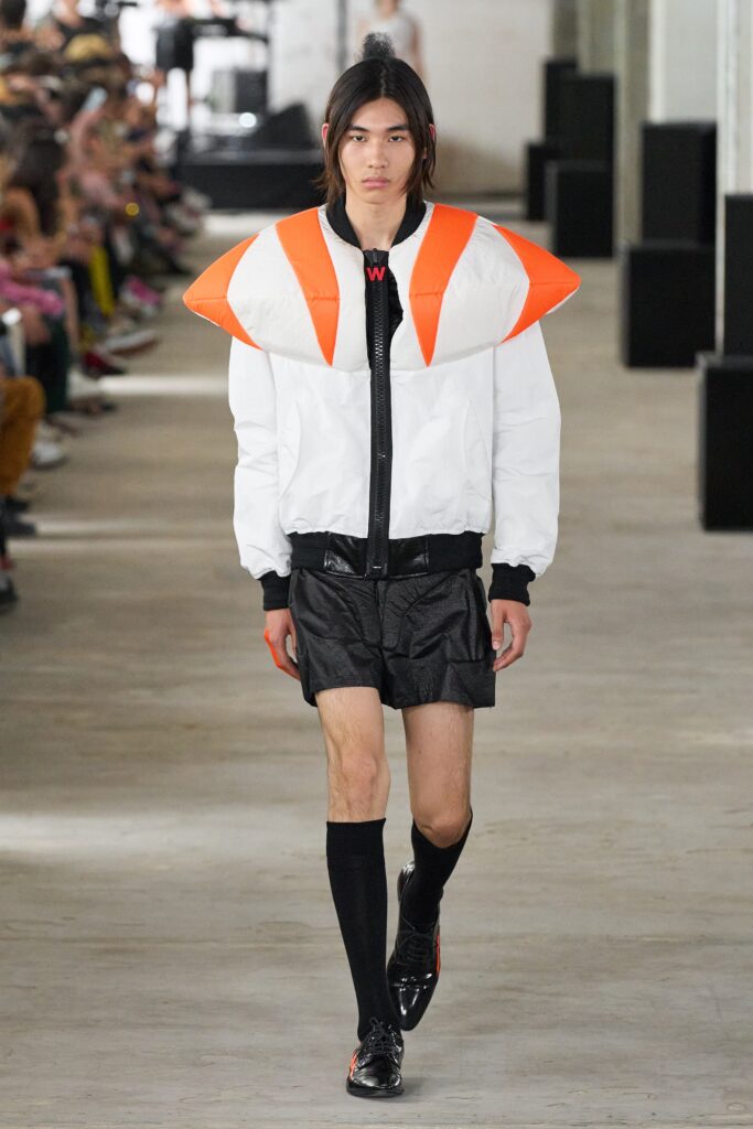 A fitted white and orange color-blocked jacket paired with black leather shorts.
