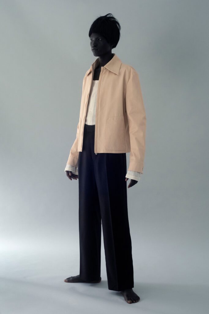 A relaxed beige cotton jacket with long sleeves paired with straight-leg black pants.