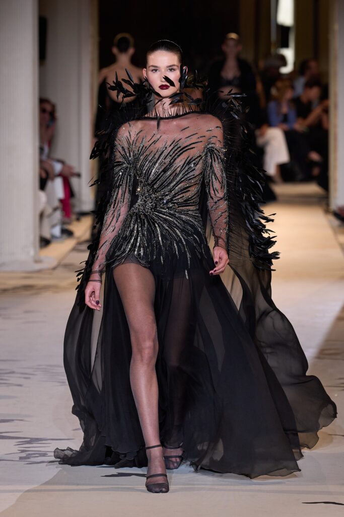 A fitted black silk dress with long sleeves, a V-neckline, and an asymmetric layered design.