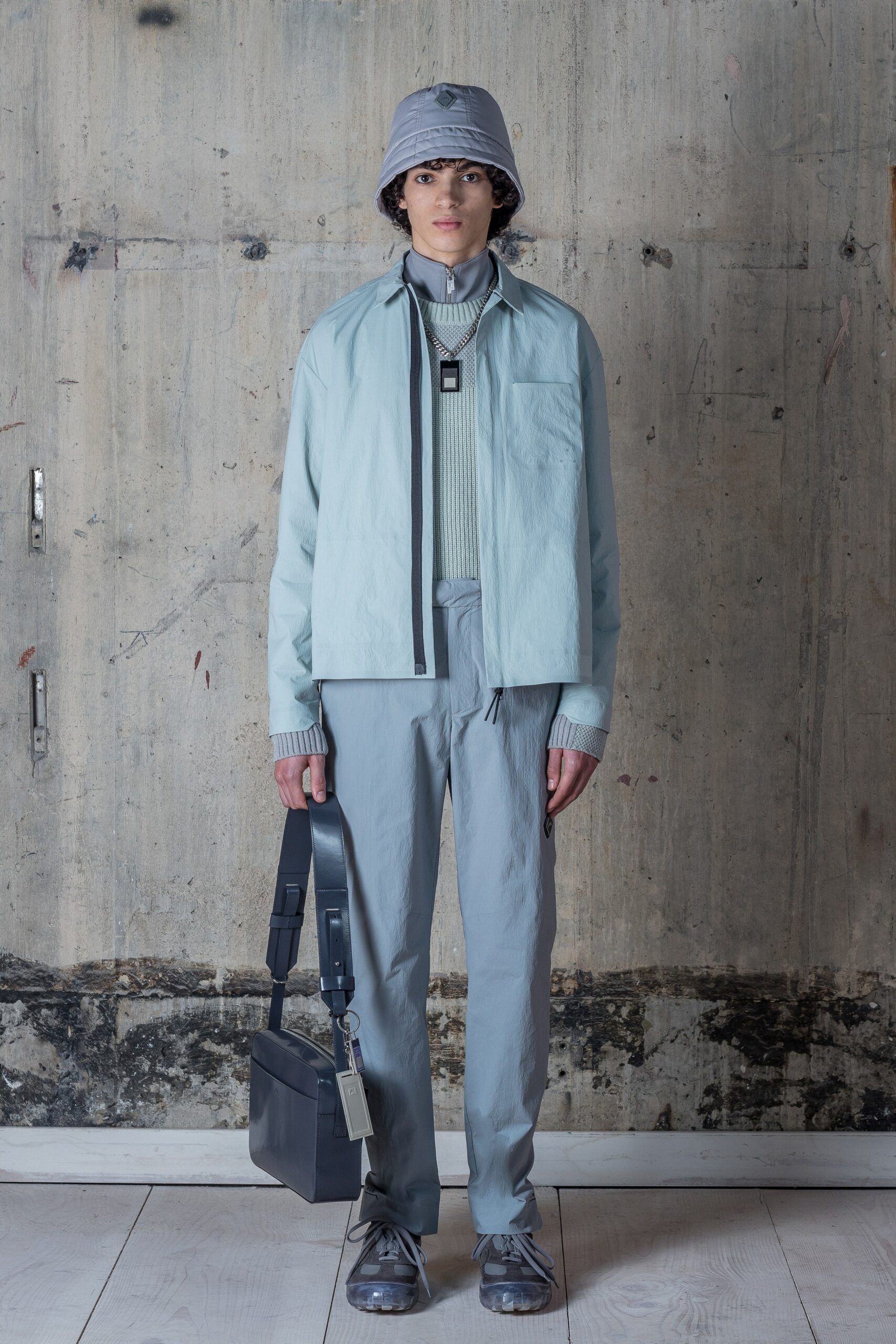 This relaxed jacket in a soft blue cotton features a collared design and a zippered front, creating a contemporary silhouette. Paired with straight-leg pants, the ensemble offers a harmonious blend of comfort and modernity, perfect for an urban setting.