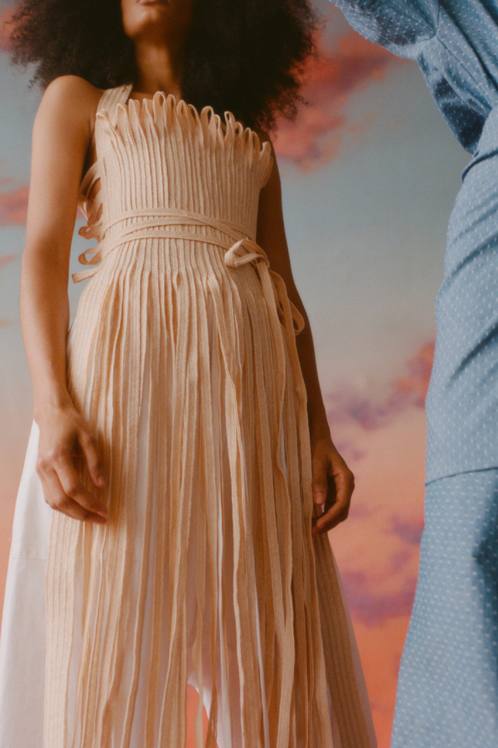 This relaxed sleeveless dress features an intricate pleated design that cascades into a tiered silhouette. The high neckline adds a touch of sophistication, while the flowing fabric creates a sense of movement and lightness.