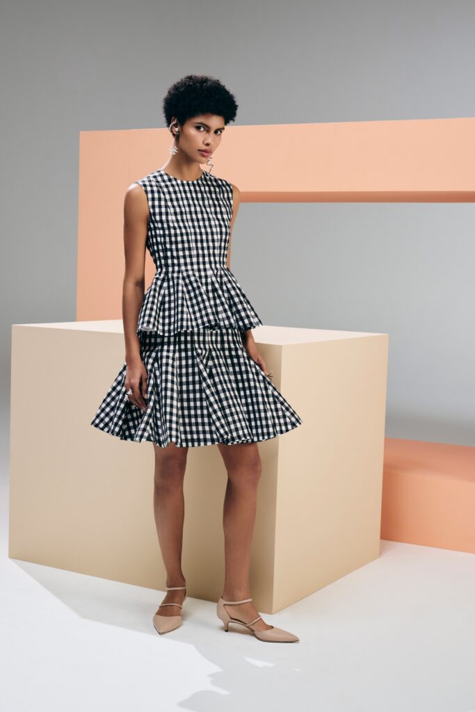 A fitted sleeveless dress in black and white check pattern with a pleated design.