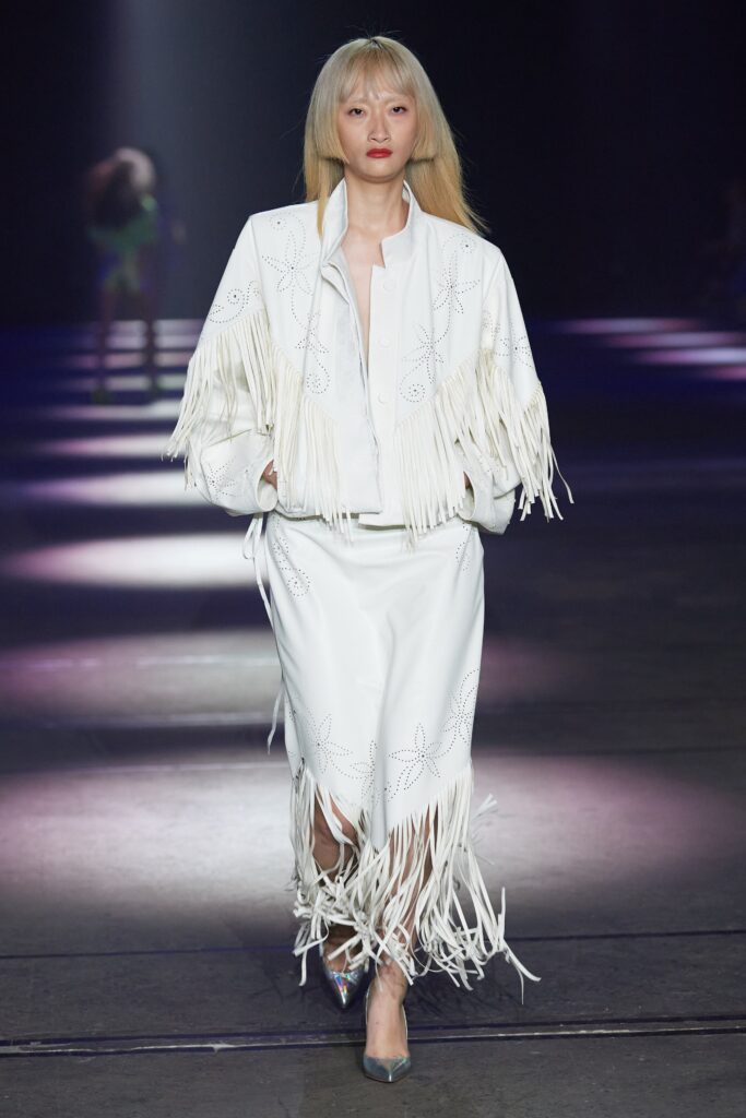 A fitted white leather jacket with fringes and an embroidered skirt, creating a stylish runway look.