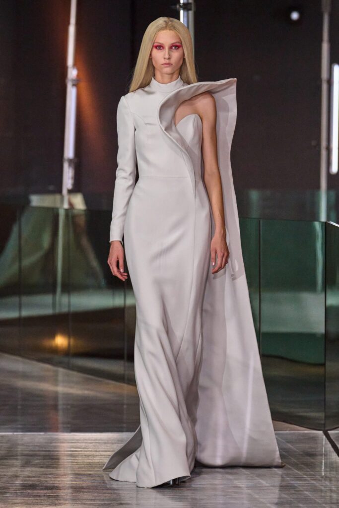 A fitted white silk gown with long sleeves, high neckline, and an asymmetric design detail.
