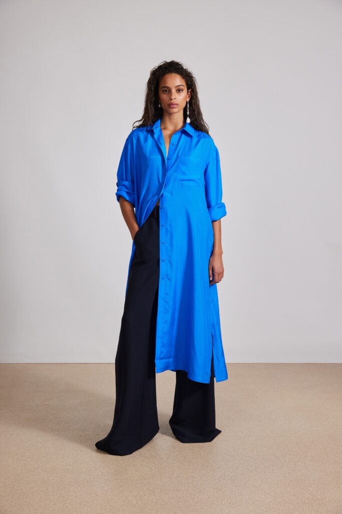 A relaxed blue shirt-dress with long sleeves and a collared neckline, paired with black pants.