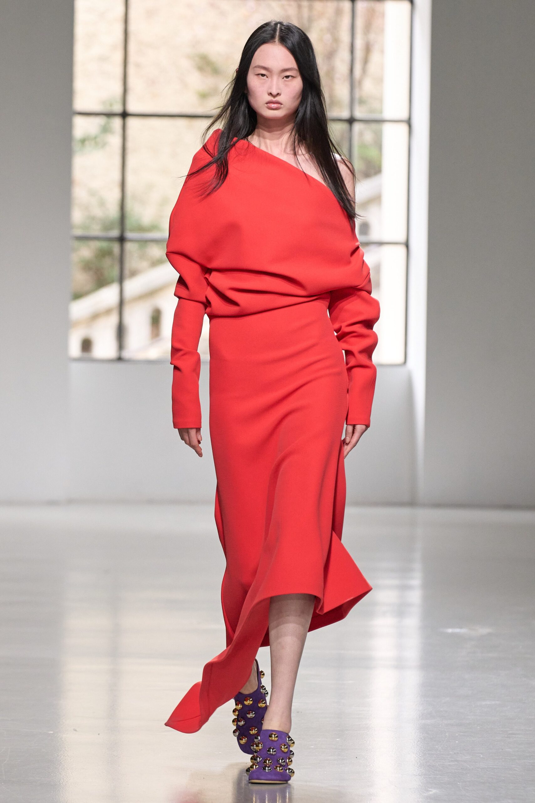 A fitted red dress with long sleeves, an off-shoulder design, and an asymmetric silhouette.