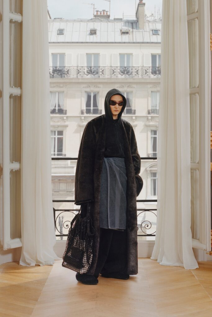 A relaxed black faux-fur coat with a hood, layered over pants.