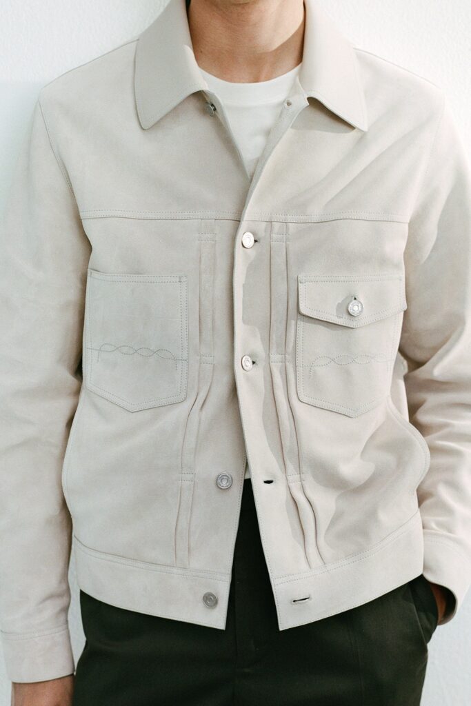 A fitted beige suede jacket with long sleeves and a collared neckline, featuring button details.