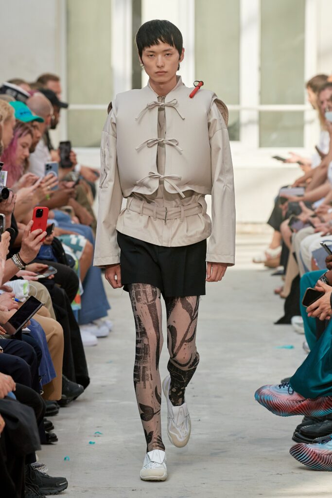 A relaxed beige jacket with long sleeves and a collared design, paired with printed black shorts.