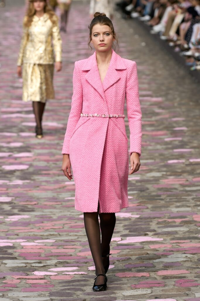 A fitted pink coat with long sleeves and a collared neckline, featuring button details.