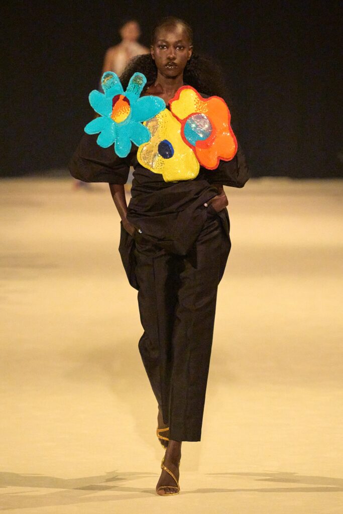 A relaxed black top featuring vibrant multicolor floral details paired with black pants.