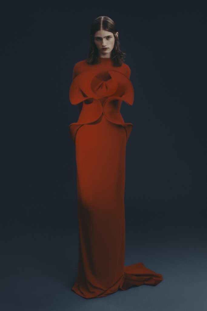 A fitted red silk gown with long sleeves and an asymmetric design detail.