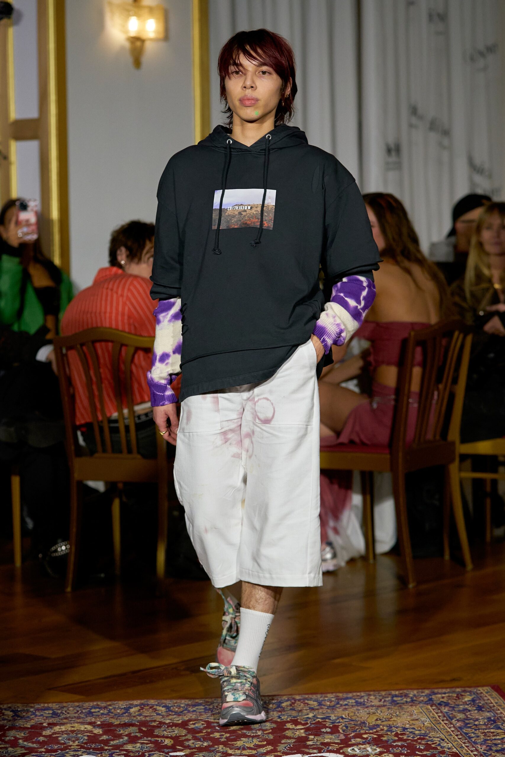 A relaxed black hoodie with long sleeves paired with white printed shorts.