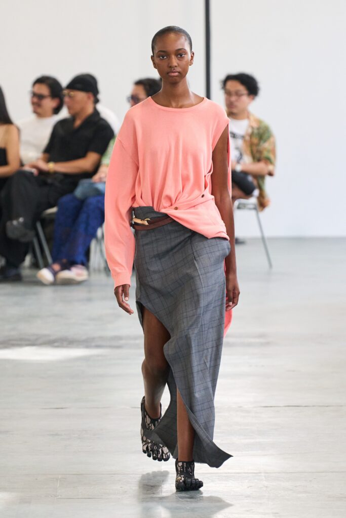 A relaxed pink long-sleeve top paired with a high-waisted gray asymmetric skirt.