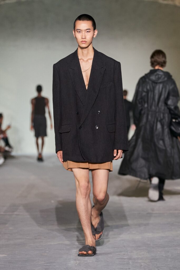 An oversized black blazer worn over a beige dress featuring a V-neckline and asymmetric design.