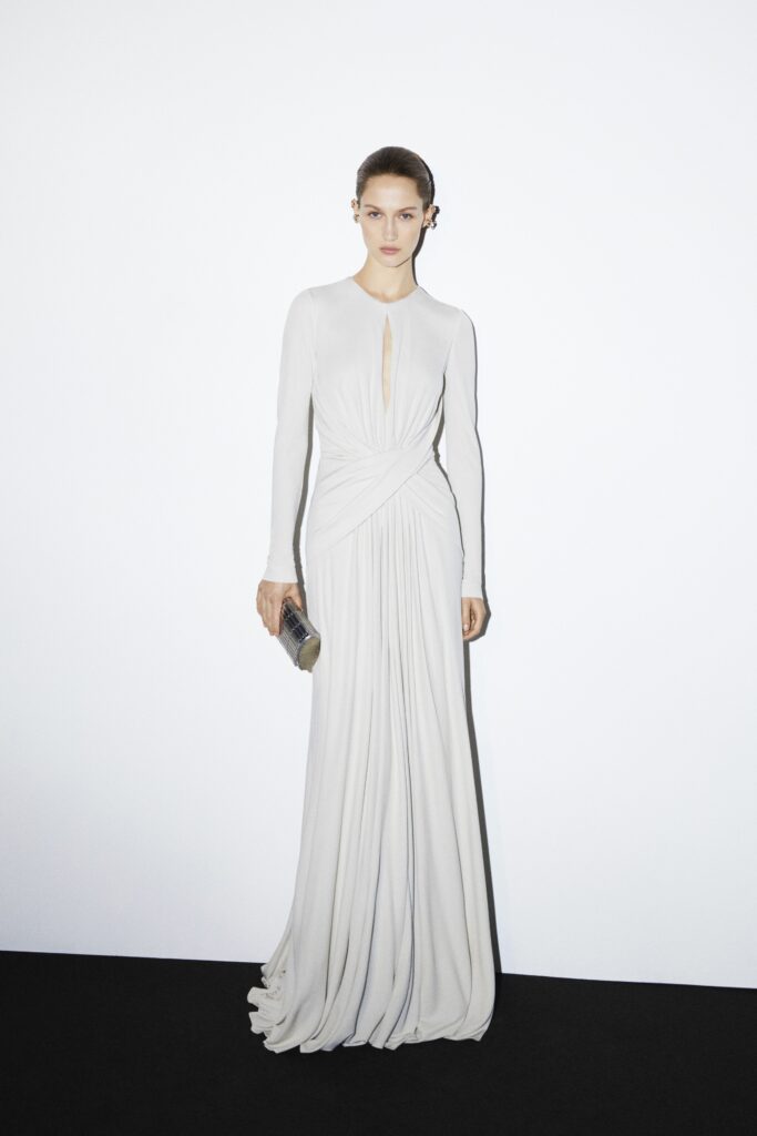 A fitted white silk gown with long sleeves, a V-neckline, and draped detailing.