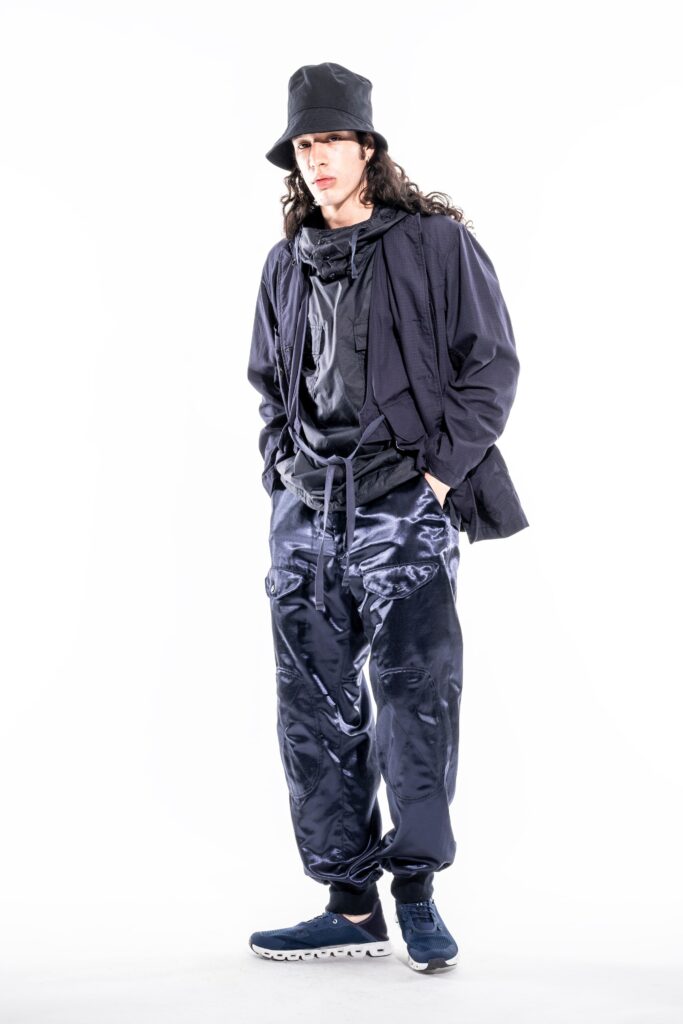 A relaxed black jacket paired with navy pants featuring a layered design and zippered details.
