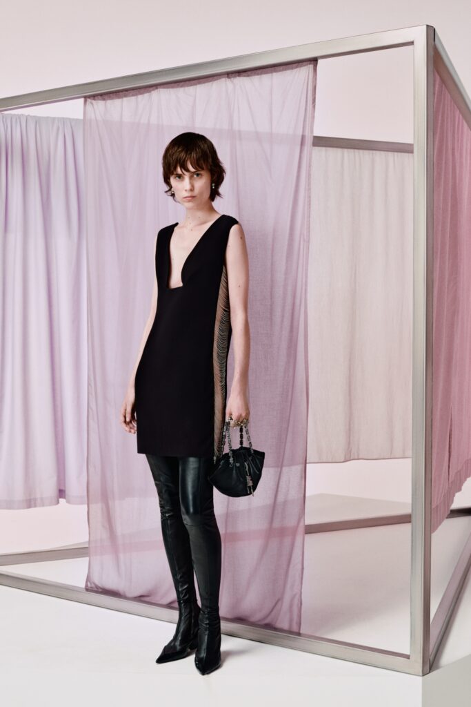 This fitted sleeveless dress in black leather features a striking V-neckline and an asymmetric design that adds a contemporary edge. Paired with sleek fitted pants, the ensemble creates a bold silhouette that plays with proportion and structure, making a statement in any setting.