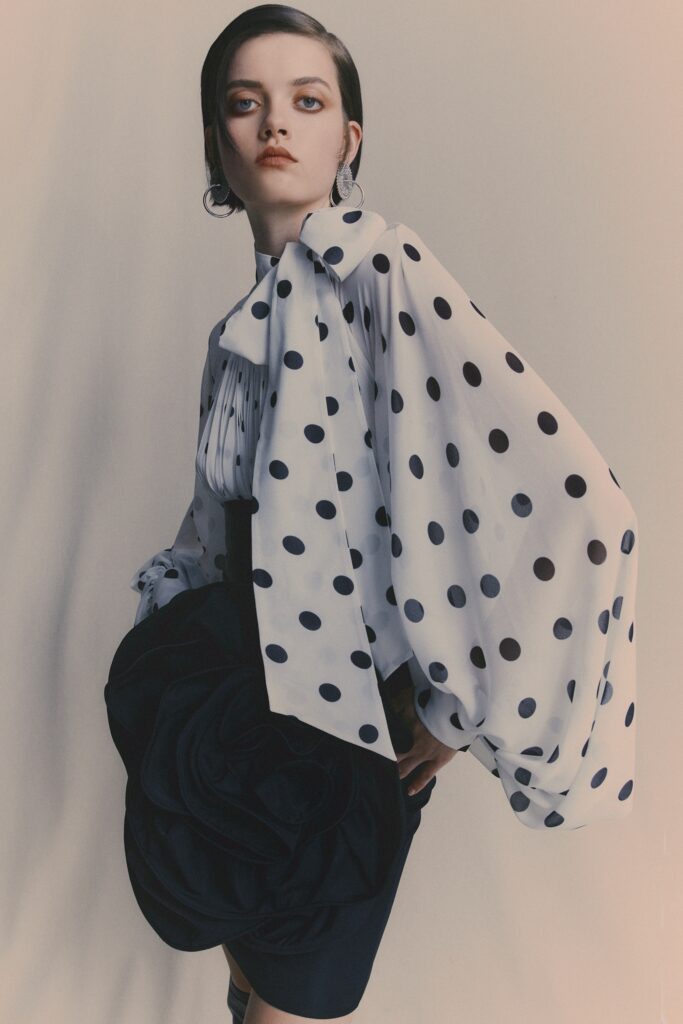 A fitted white polka-dot blouse with long sleeves and a collared neckline, paired with a fitted skirt.