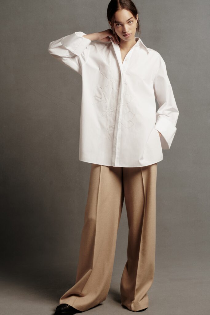 A relaxed white long-sleeve collared shirt paired with wide-leg beige pants featuring embroidery.