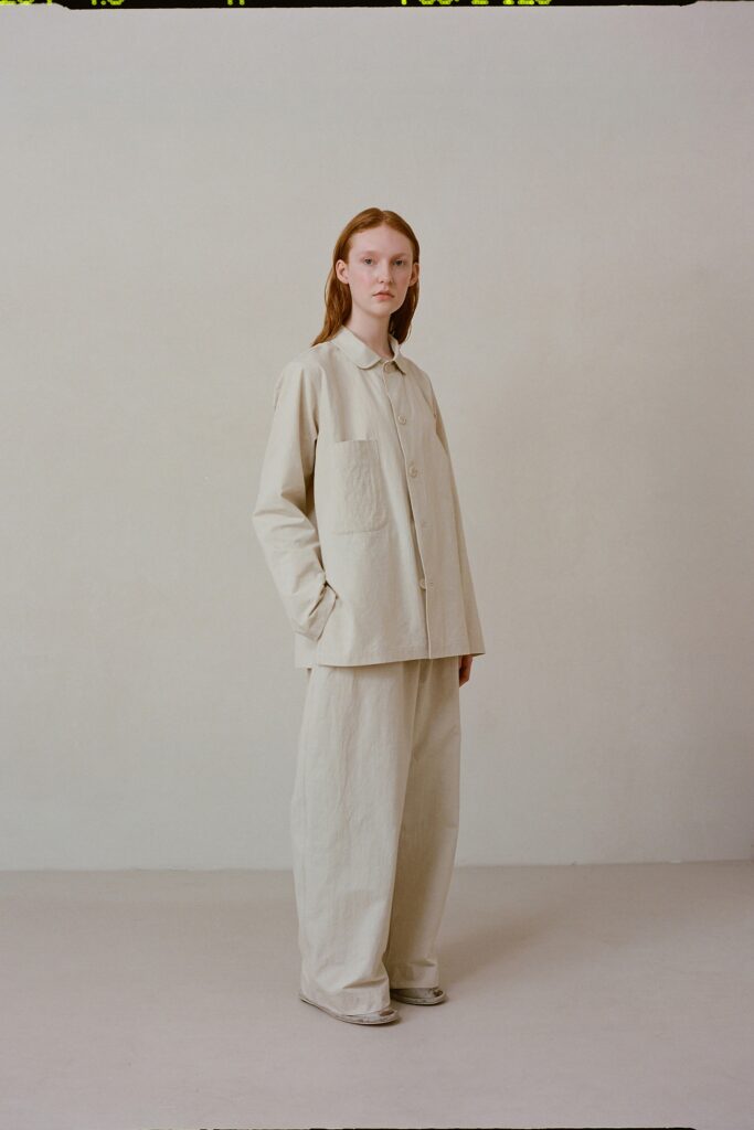 A relaxed beige cotton jacket with long sleeves and collared neckline paired with straight-leg pants.